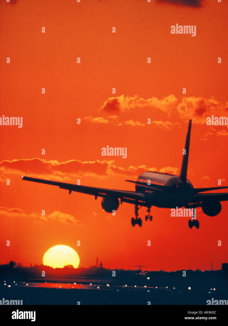 Boeing 757 jet in the air runway lights heading into an golden orange sky at sunset sunrise dusk showing jet thrust exhaust poll Stock Photo