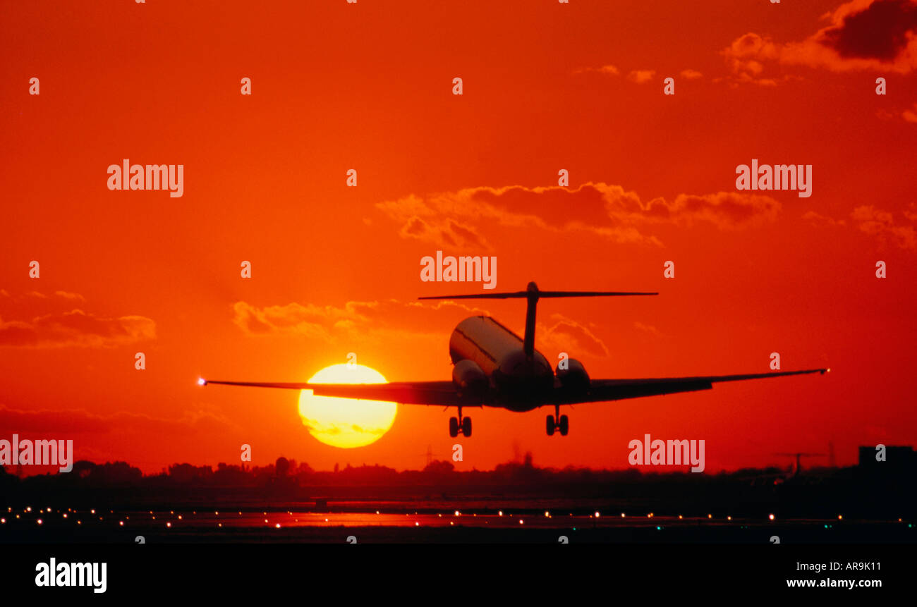 Regional Jet MD-80 jet air runway lights flying golden orange sky at sunset sunrise dusk jet thrust exhaust Stock Photo