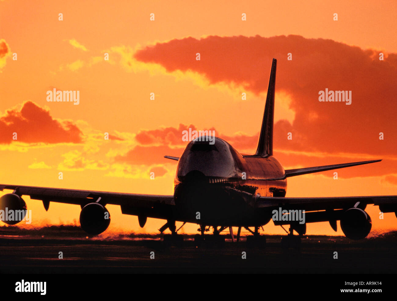 Boeing 747 jumbo jet on the runway with an golden orange sky at sunset sunrise dusk showing jet thrust exhaust pollution clouds Stock Photo