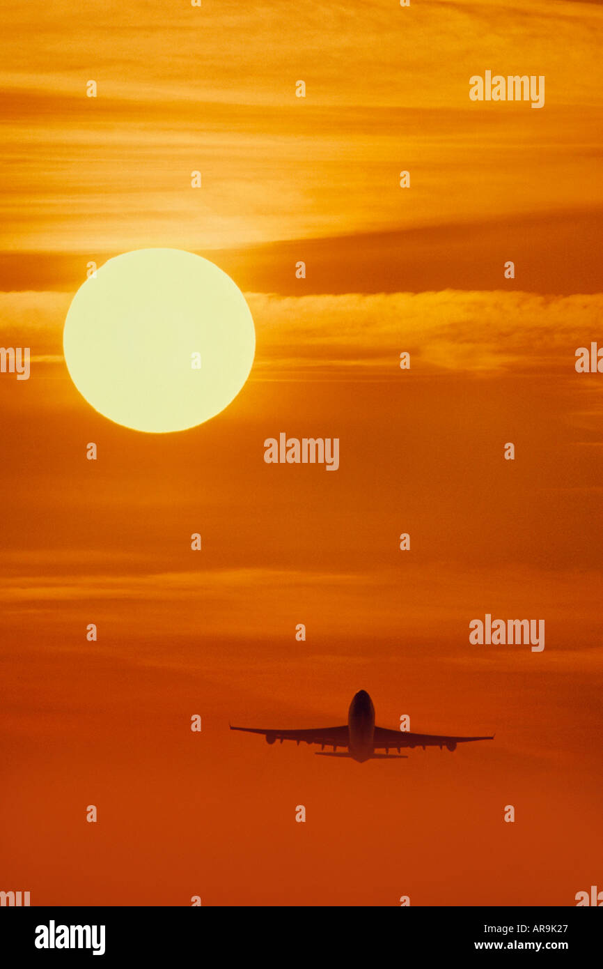 airliner Boeing 747 jumbo jet flying golden orange cloud sky at sunset sunrise dusk showing jet thrust exhaust Stock Photo