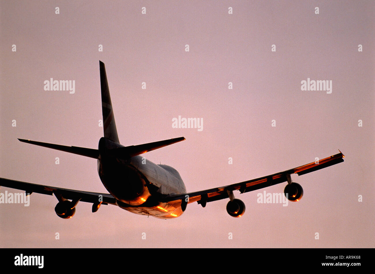 Boeing 747 in the air flying into an pink purple sky at sunset sunrise dusk showing jet thrust exhaust pollution wing Stock Photo