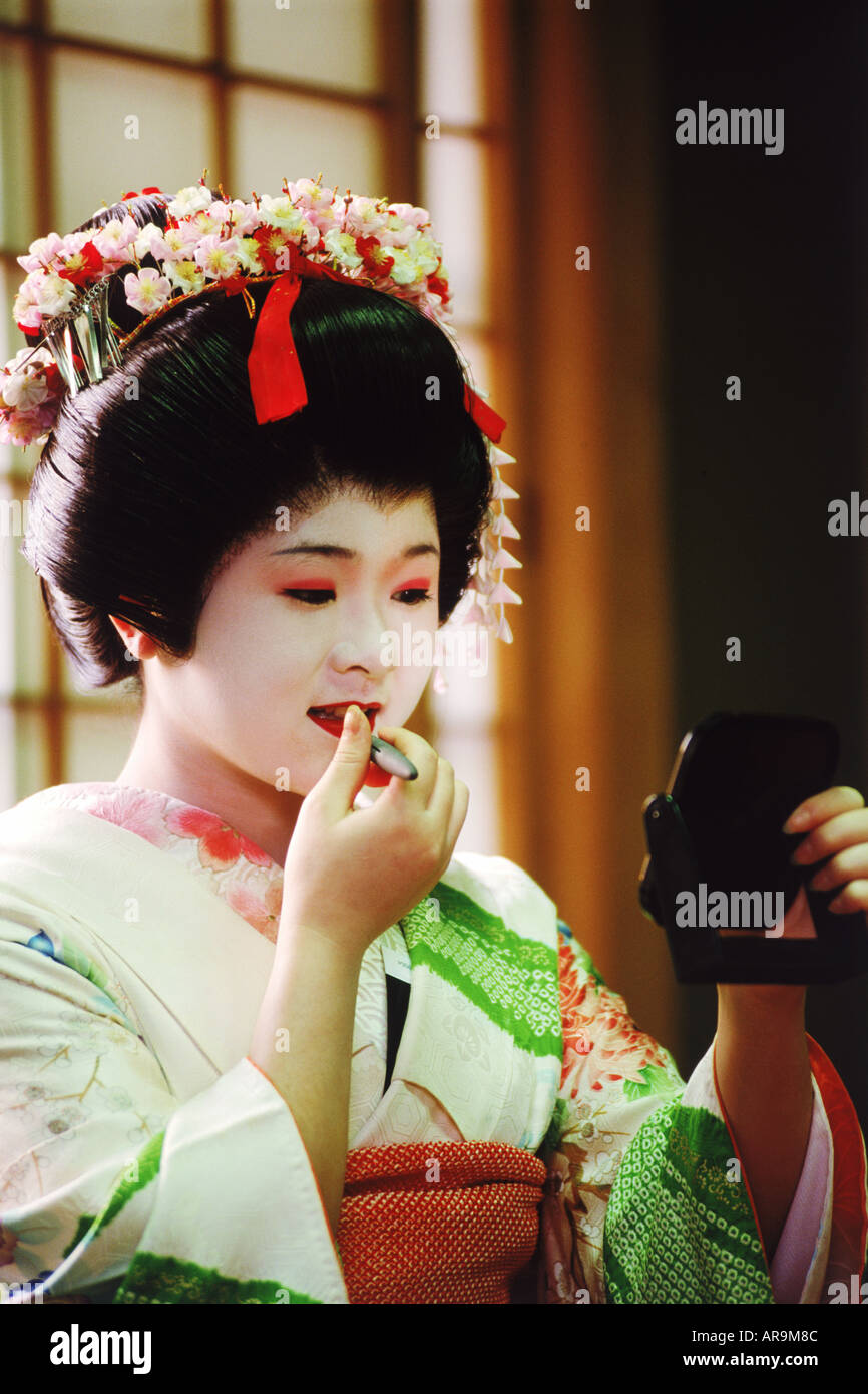 Geisha using small mirror to apply make up at home Stock Photo