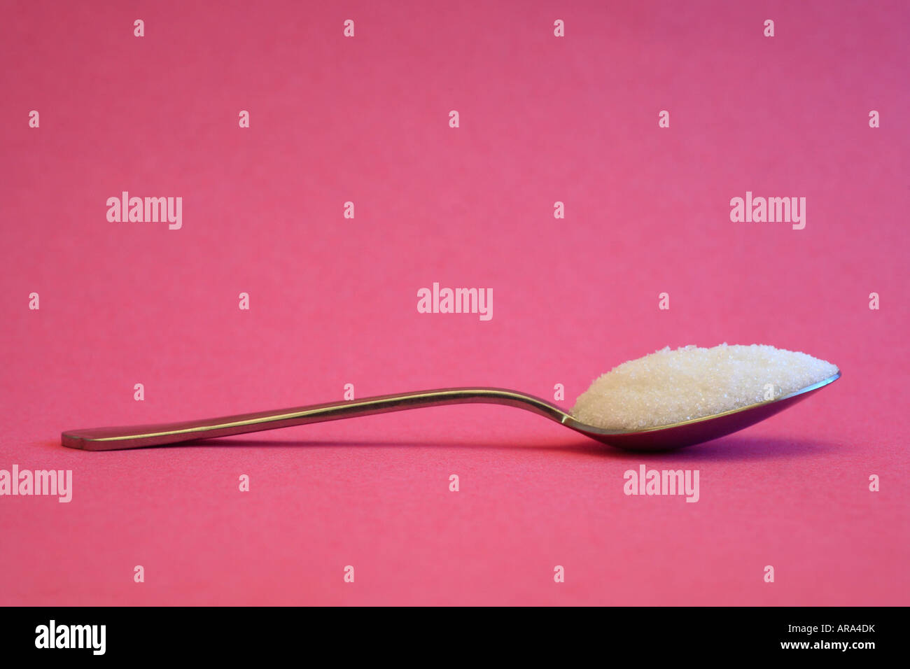 Spoonful of white sugar against a pink background. Stock Photo