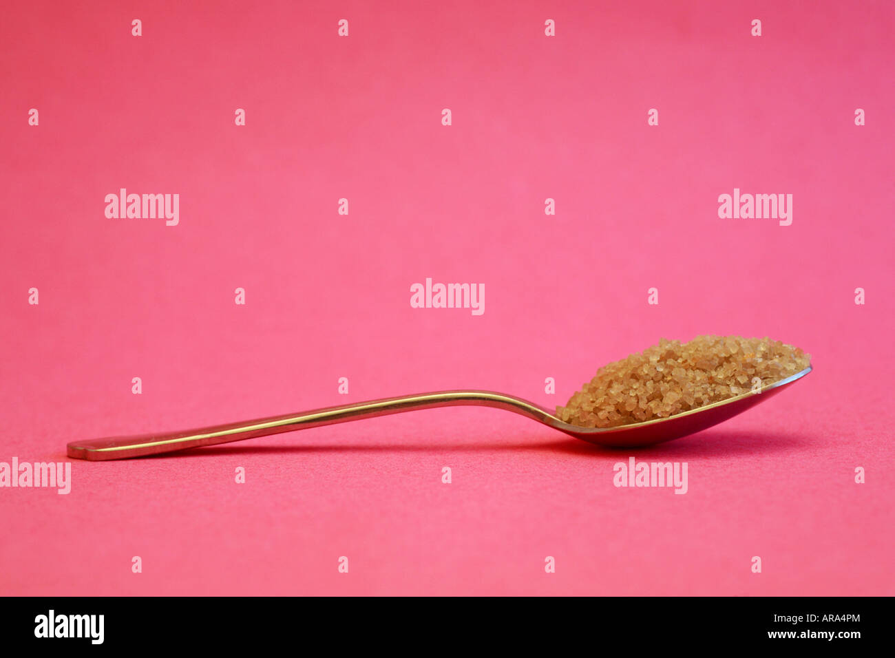 Spoonful of demerara sugar against a pink background. Stock Photo