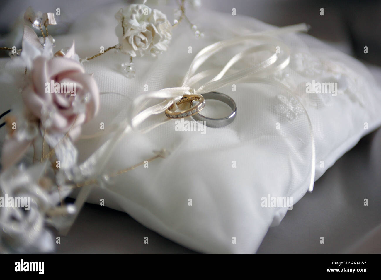 Bride and grooms wedding rings on white cushion with bouquet of flowers Stock Photo
