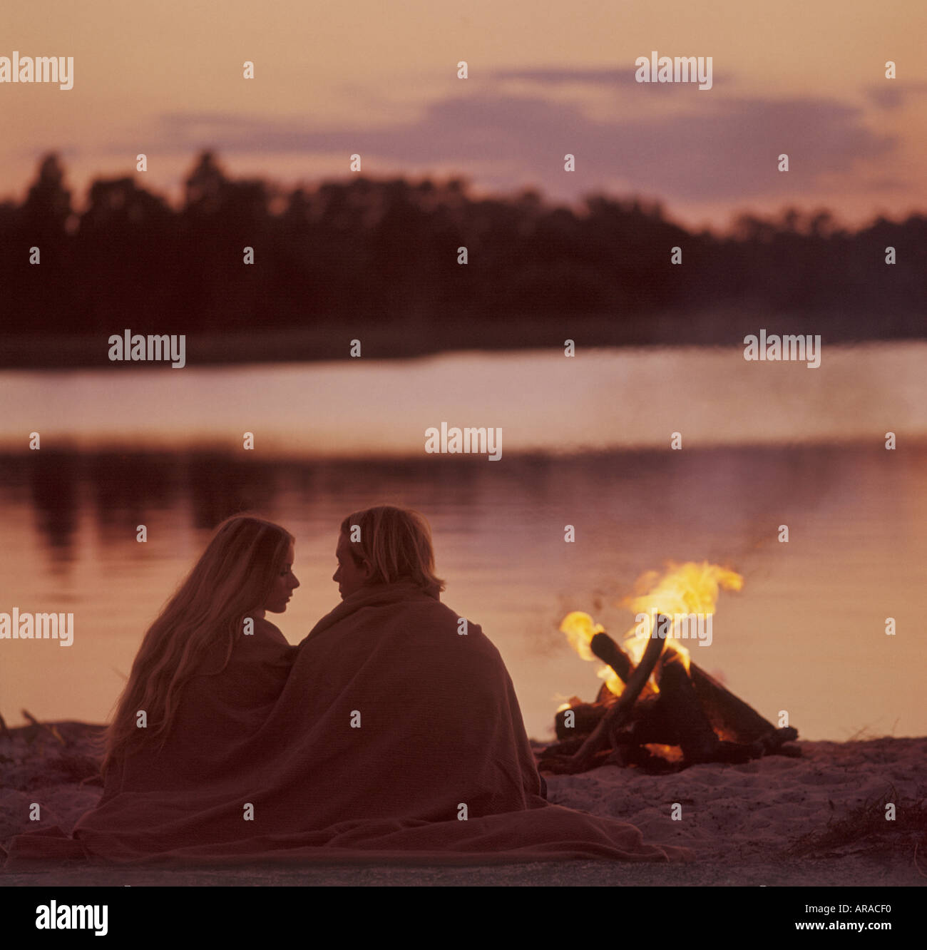 romantic couple relaxing by campfire on beach Stock Photo