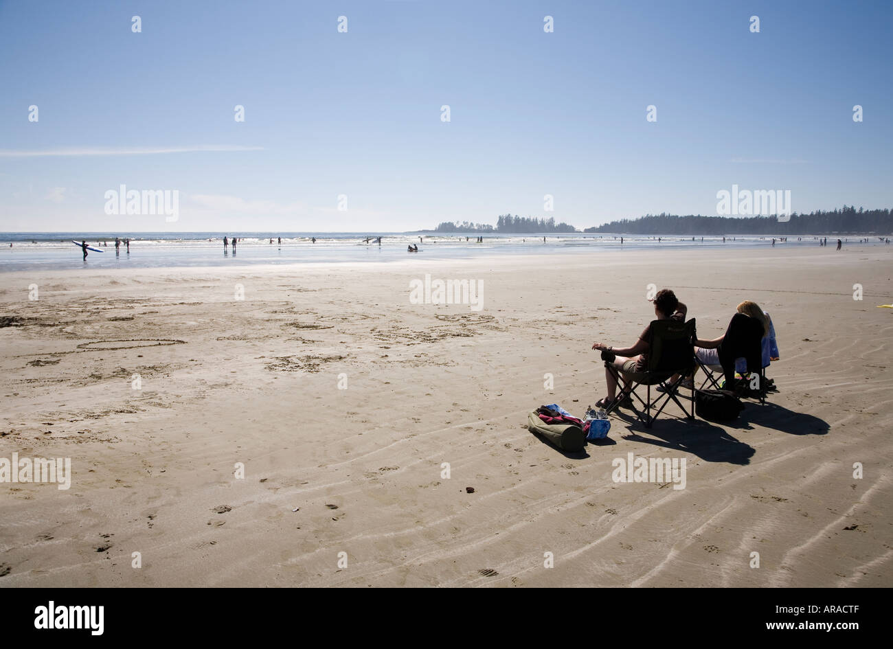 Two people in chairs watching surfers and swimmers Long Beach Pacific Rim national park reserve Vancouver island Canada Stock Photo