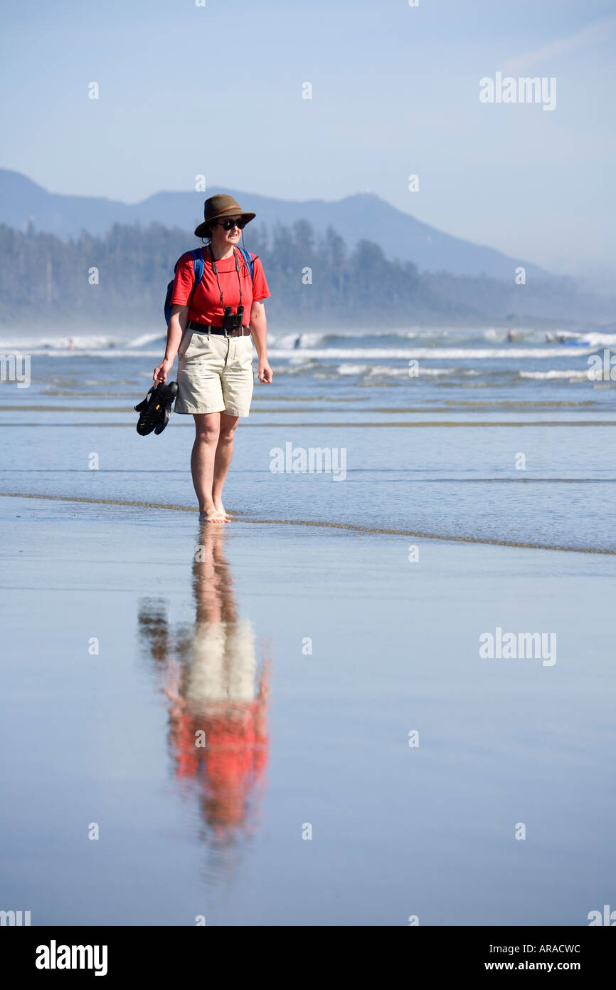 Woman walking barefoot in shallows carrying sandals Long Beach Pacific Rim national park reserve Vancouver island Canada Stock Photo