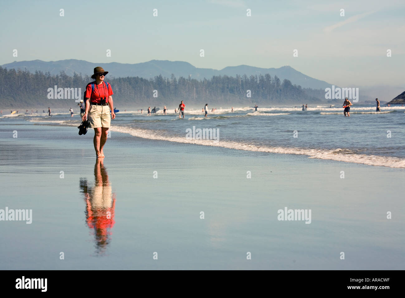 Woman walking barefoot in shallows carrying sandals Long Beach Pacific Rim national park reserve Vancouver island Canada Stock Photo