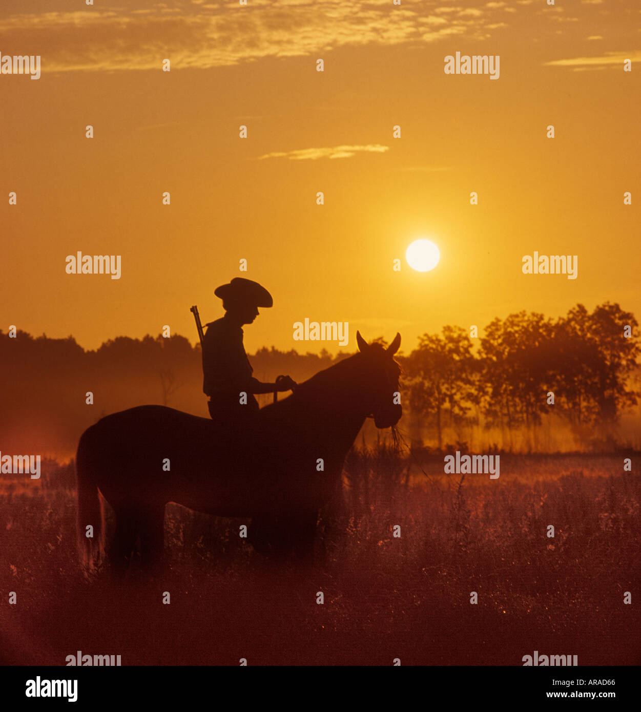man with rifle on horseback riding at sunset Stock Photo