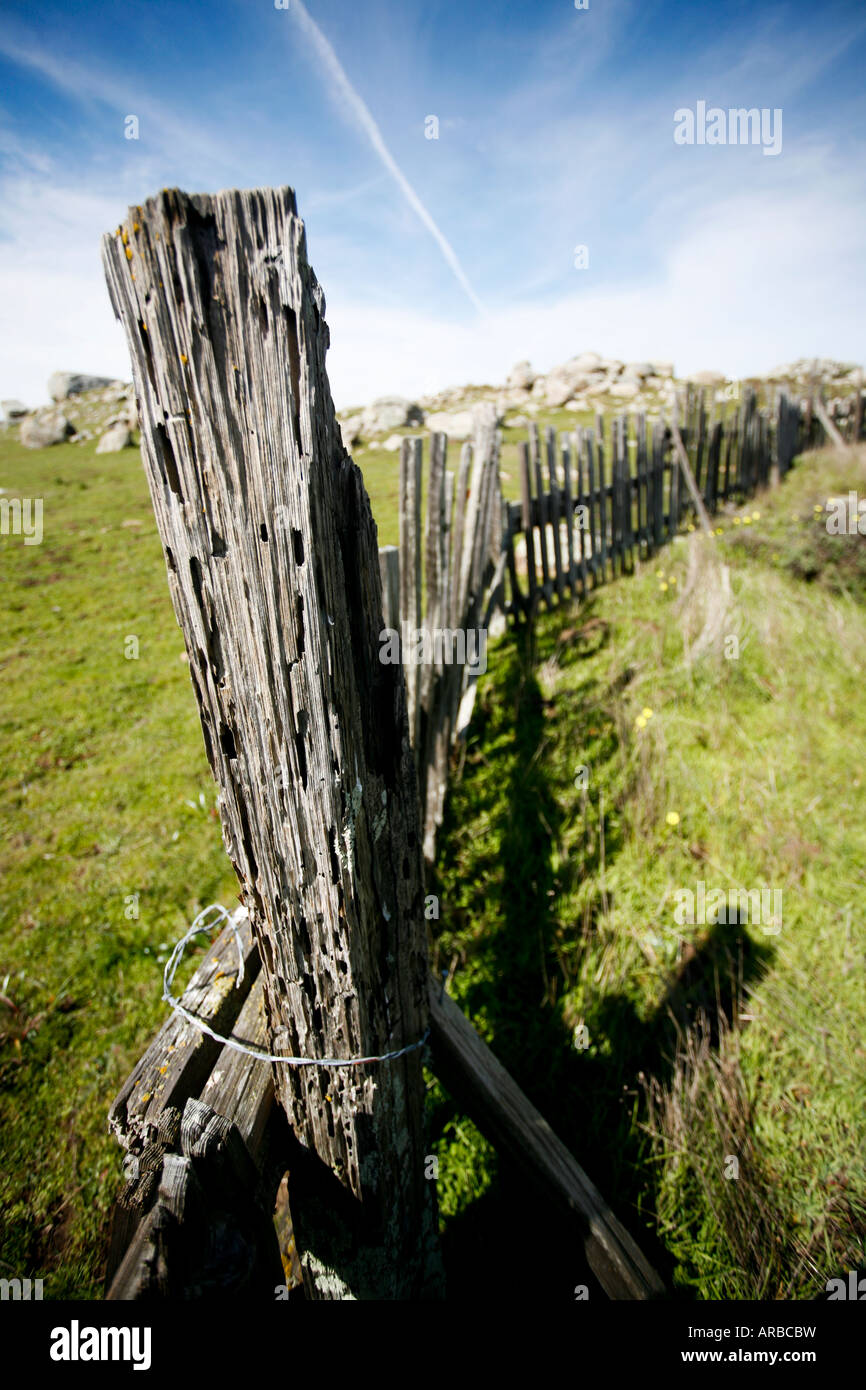 Worn down wooden fence along a grassy knoll with large boulders in the background Stock Photo