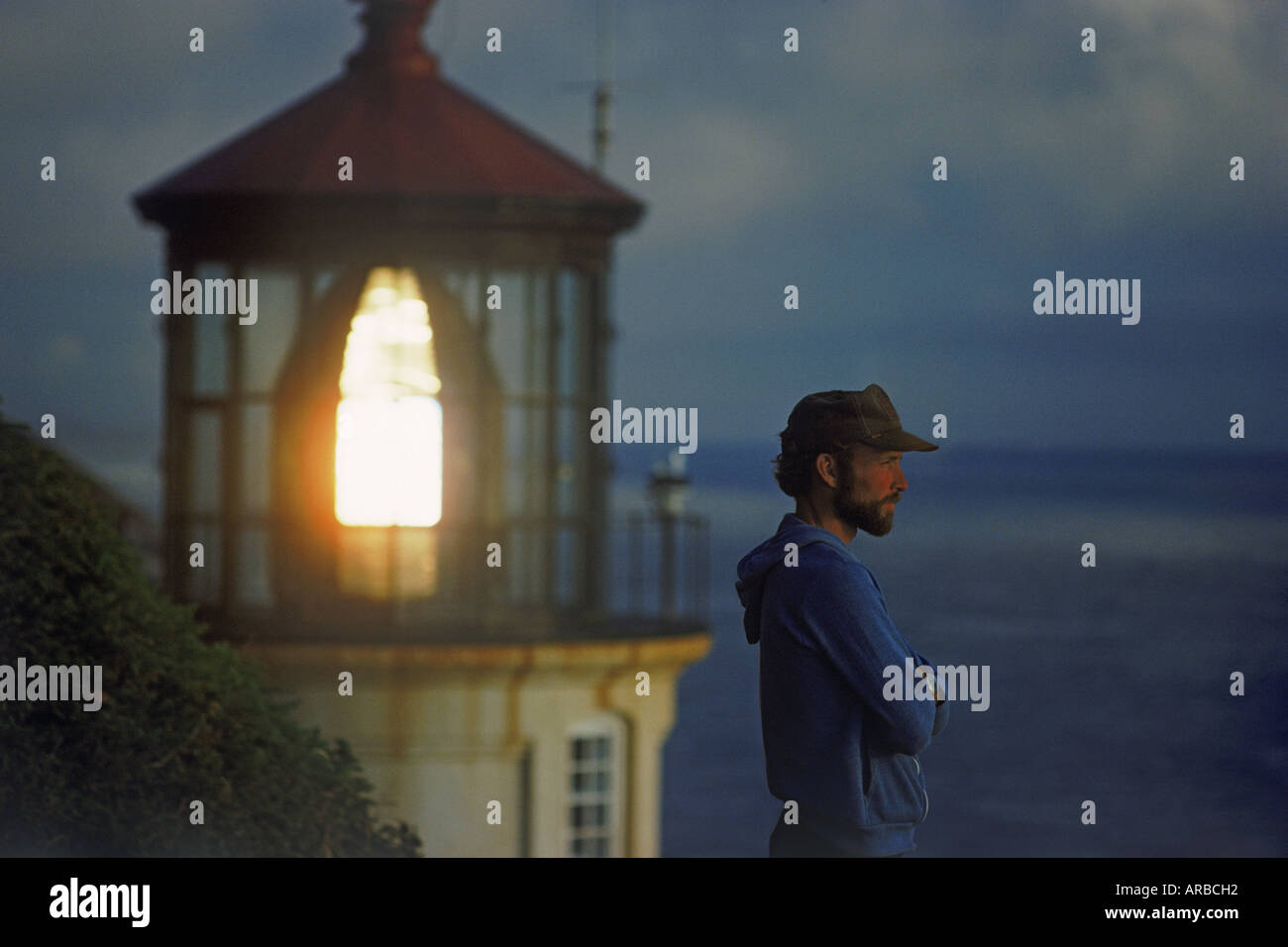 Man standing at dusk on bluff above Pacific Ocean with Heceta Head Lighthouse near Florence, Oregon USA Stock Photo