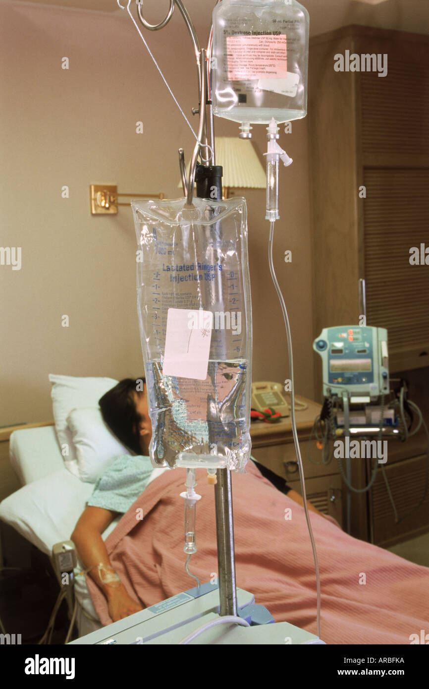 Female patient in hospital bed connected to a cocktail of fluids via an IV Stock Photo