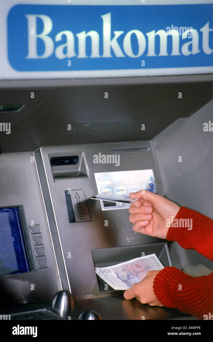 Hands holding money and debit card at ATM machine in Sweden Stock Photo