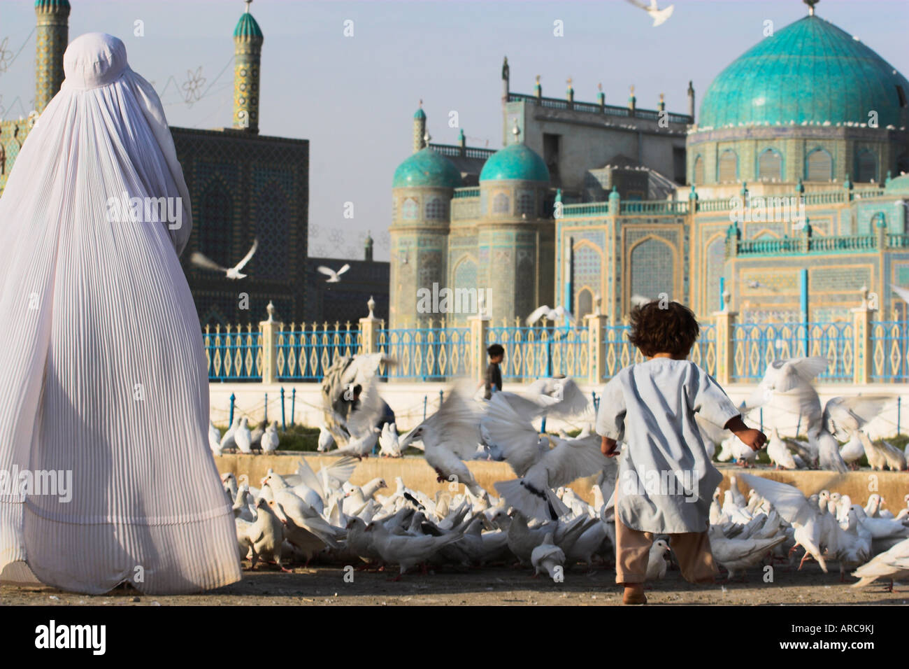 Lady in burqa feeding famous white pigeons whilst child chases them, Shrine of Hazrat Ali, Mazar-i-Sharif, Balkh, Afghanistan Stock Photo