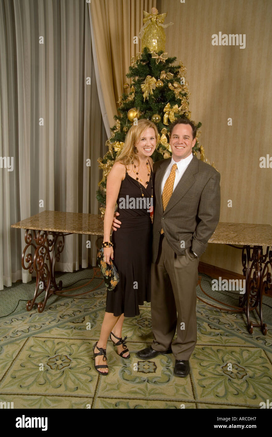 An attractive young couple pose for a formal picture in front of a Christmas tree Stock Photo