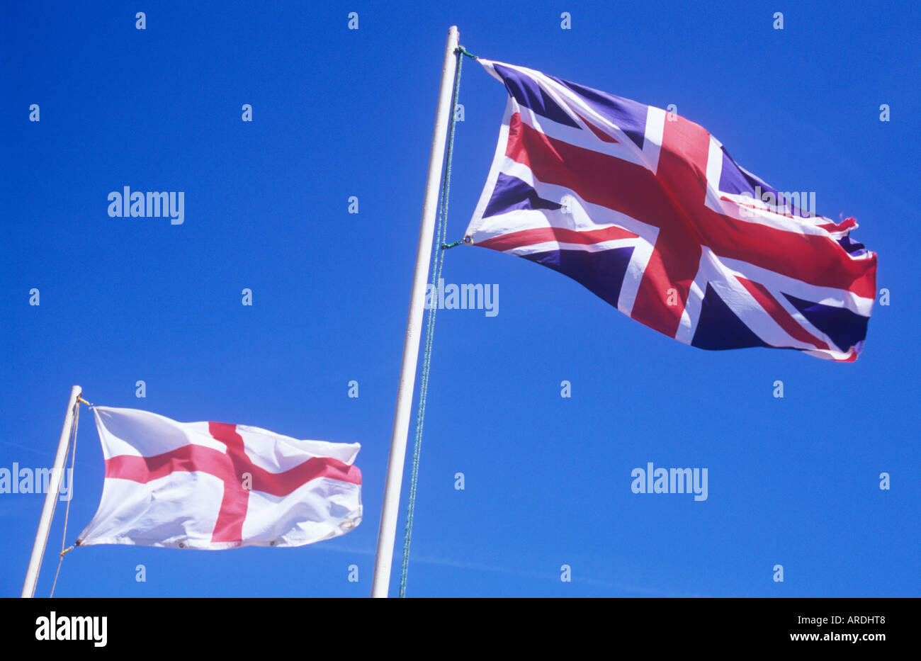 St George flag or English Ensign fluttering from flagpole against clear blue sky with Union Jack on separate pole Stock Photo