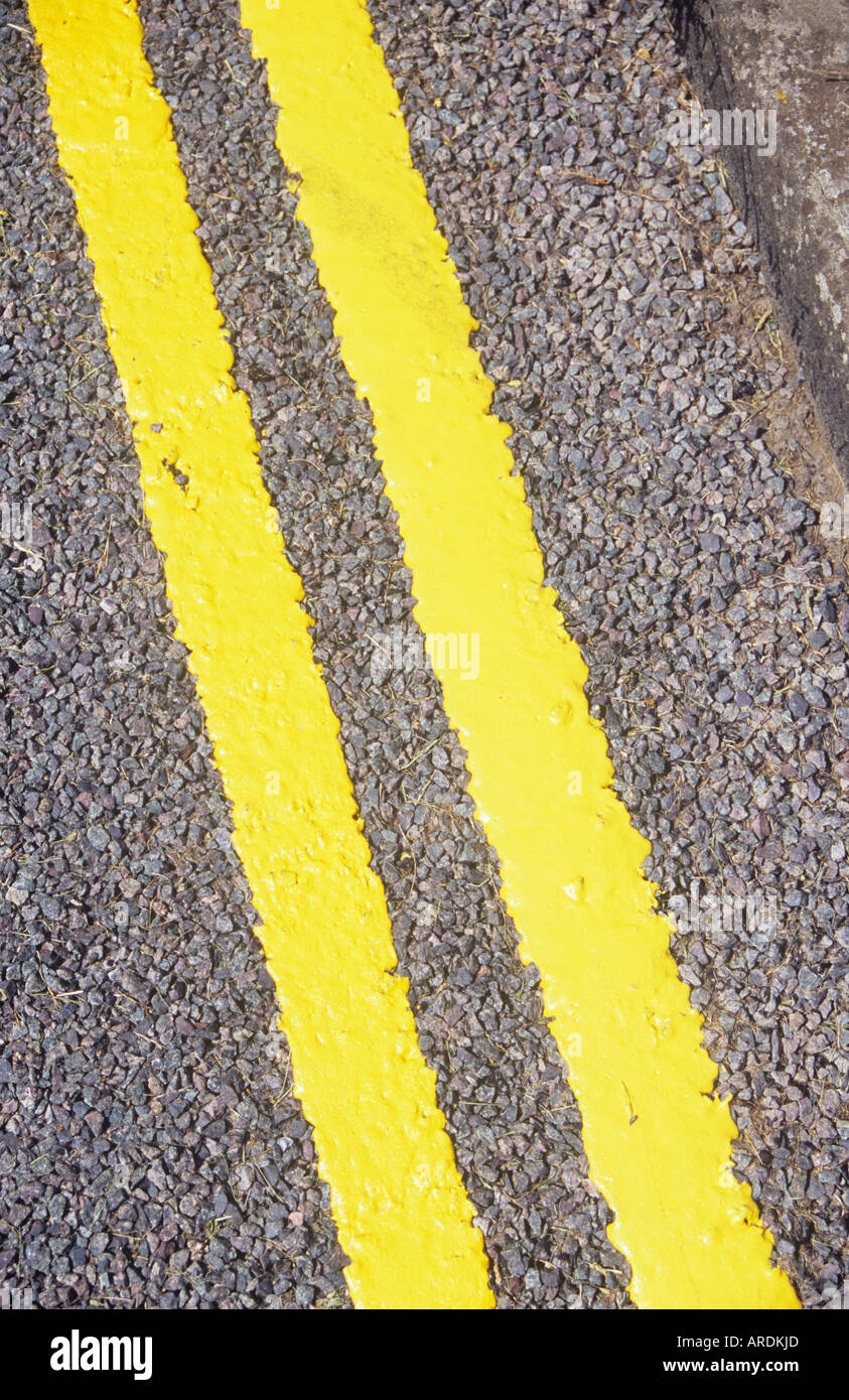 Diagonal detail from above of freshly painted double yellow lines on tarmac road with kerb Stock Photo