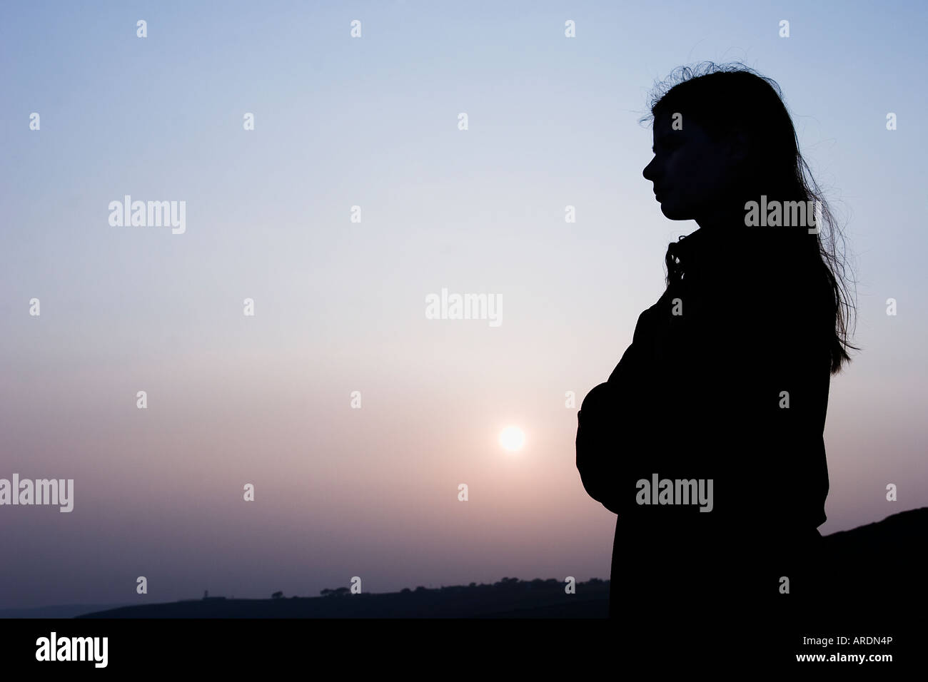 Silhouetted girl looking out to sea at sunset. Stock Photo