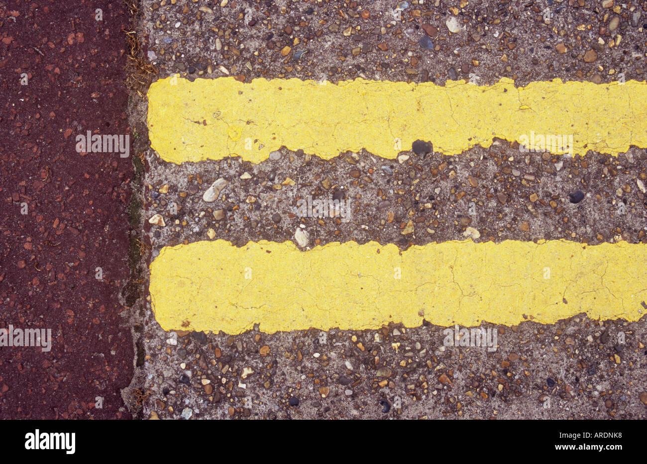 Detail from directly above of worn double yellow lines on concrete road surface and ending where they meet pink asphalt Stock Photo