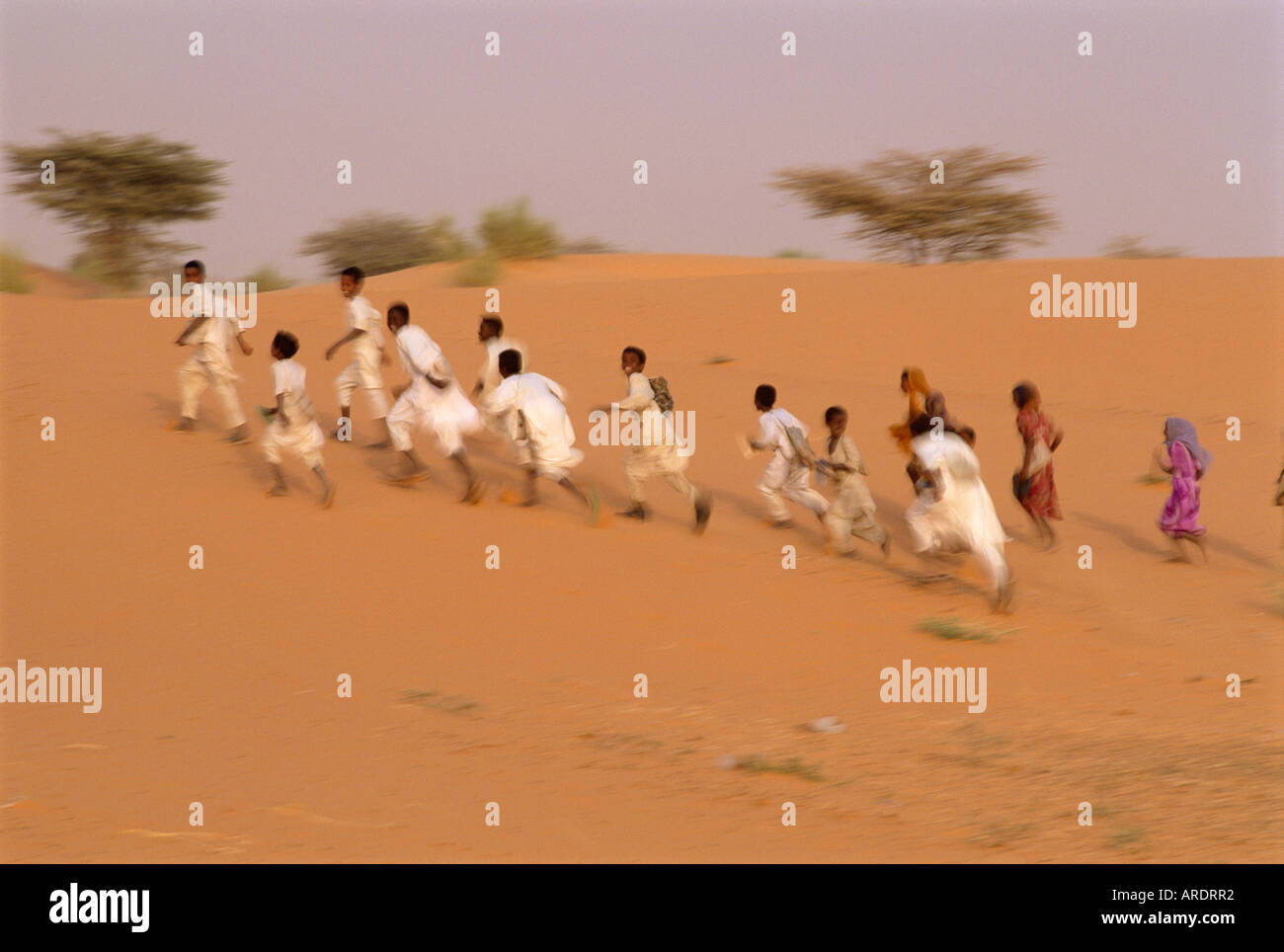 Sudanese children running across sand dune after school Um Dalam near El Obeid Sudan Stock Photo