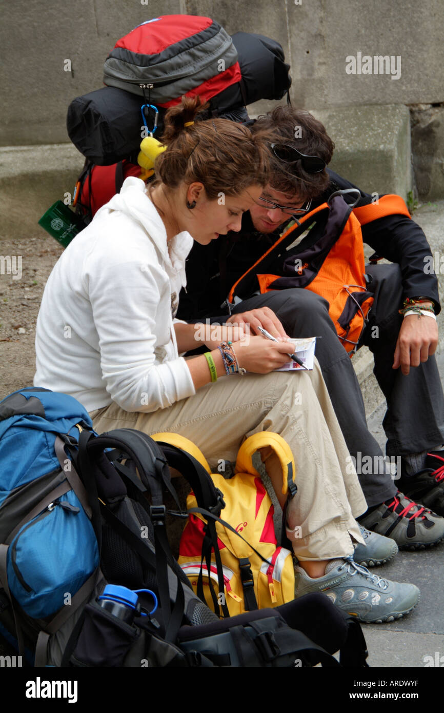 Young Backpackers Young backpackers sitting on the roadside reading a tourist guide book ...