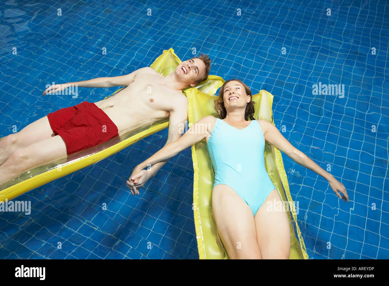 Couple lying on lylos holding hands Stock Photo