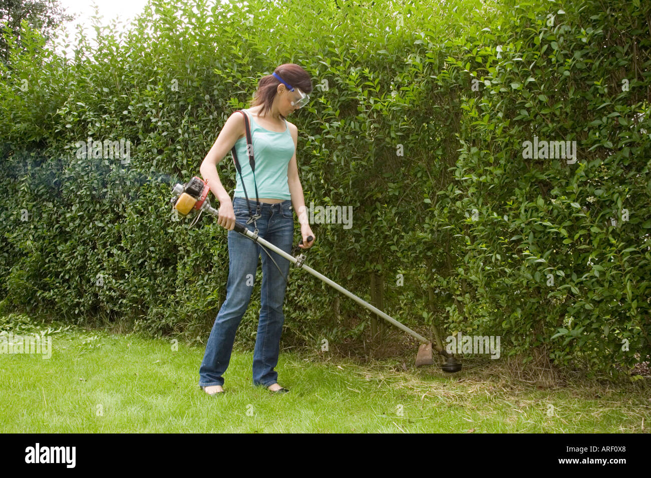 A woman using a petrol powered strimmer to cut grass and weeds Stock