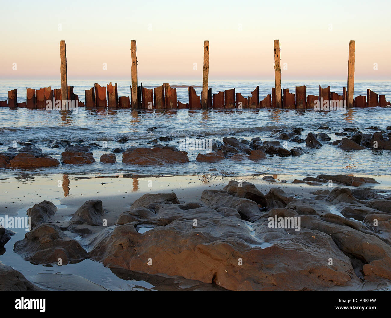 LOW TIDE ON HAPPISBURGH BEACH WITH BROKEN SEA DEFENCES REFLECTED IN WET ...