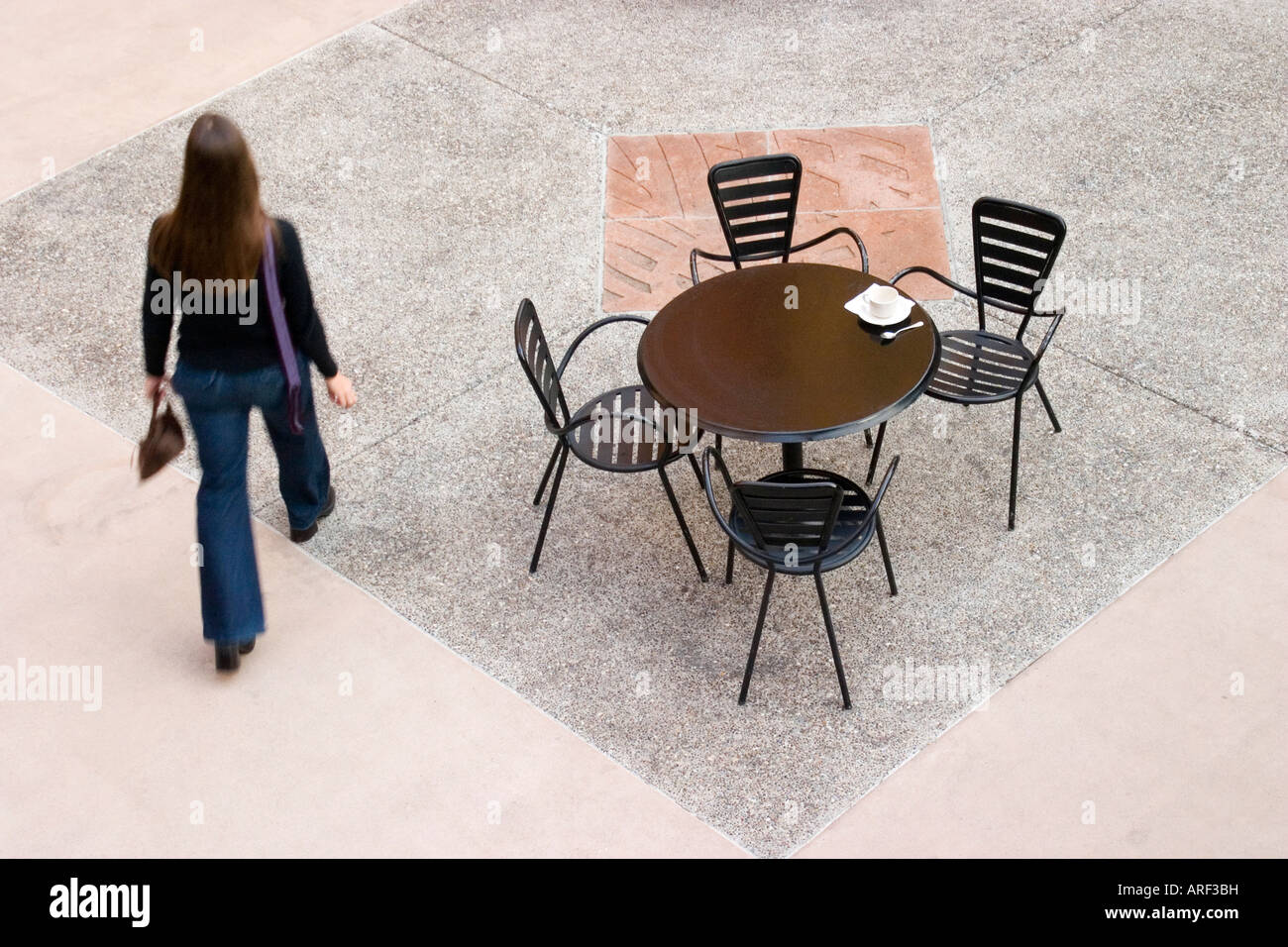 An anonymous young woman walks through an empty outdoor cafe. Stock Photo