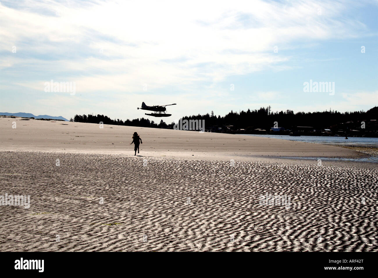 Tofino Sea-plane with silhouette of a child in the foreground running on a beach Stock Photo