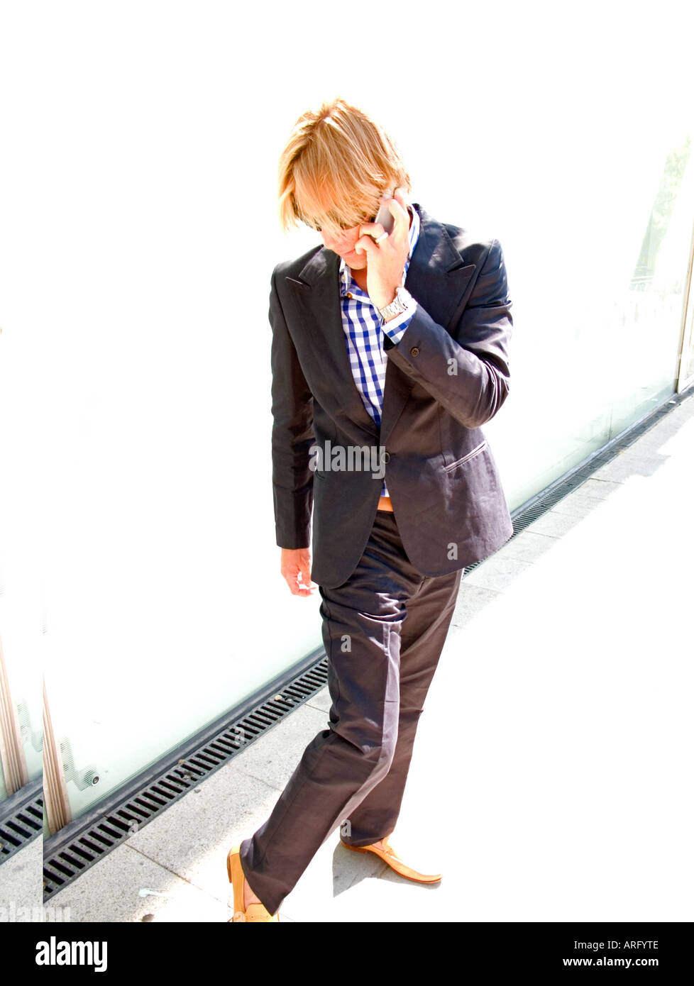 A young caucasian businessman on his mobile checks out his own footwear Stock Photo