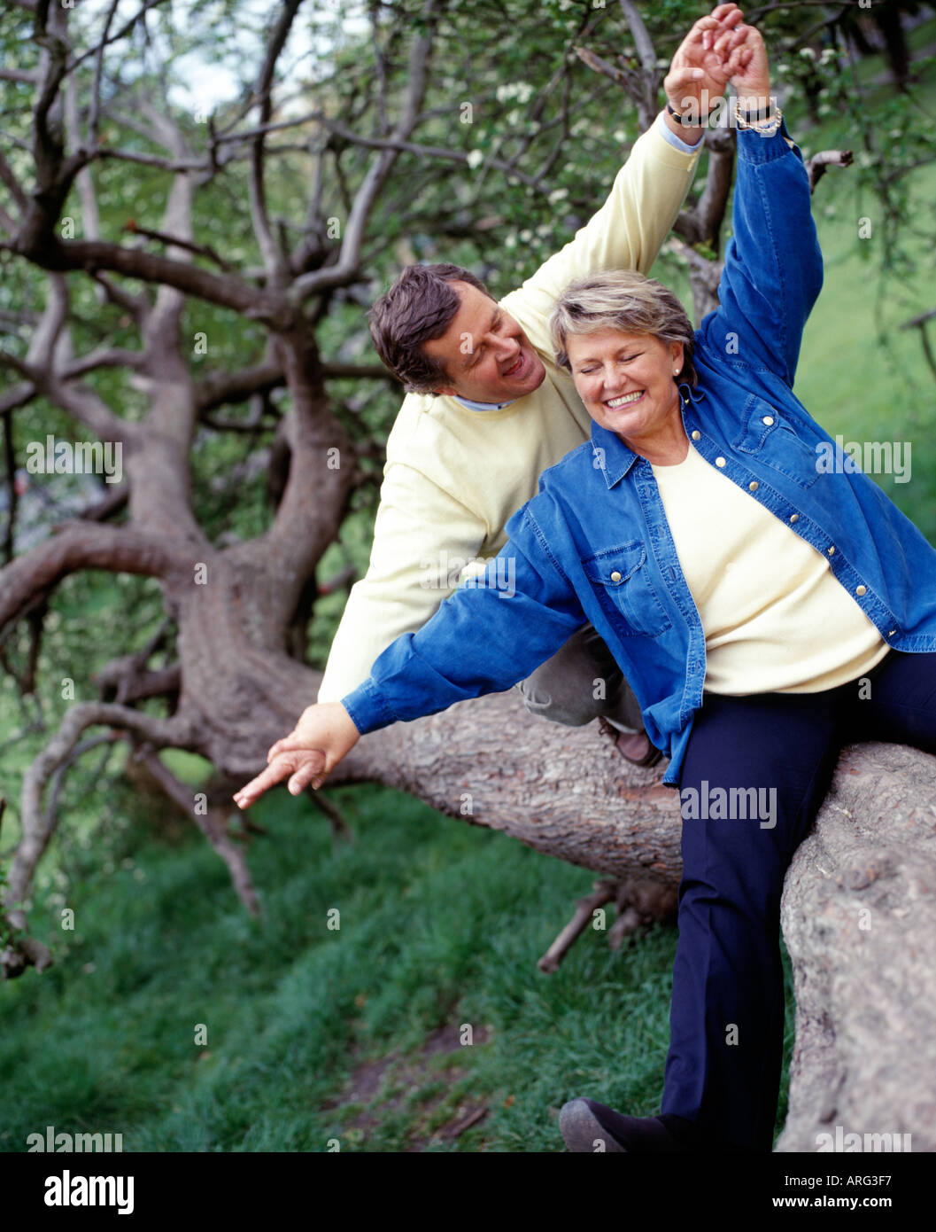 middle aged couple sitting together having fun on tree trunk Stock Photo