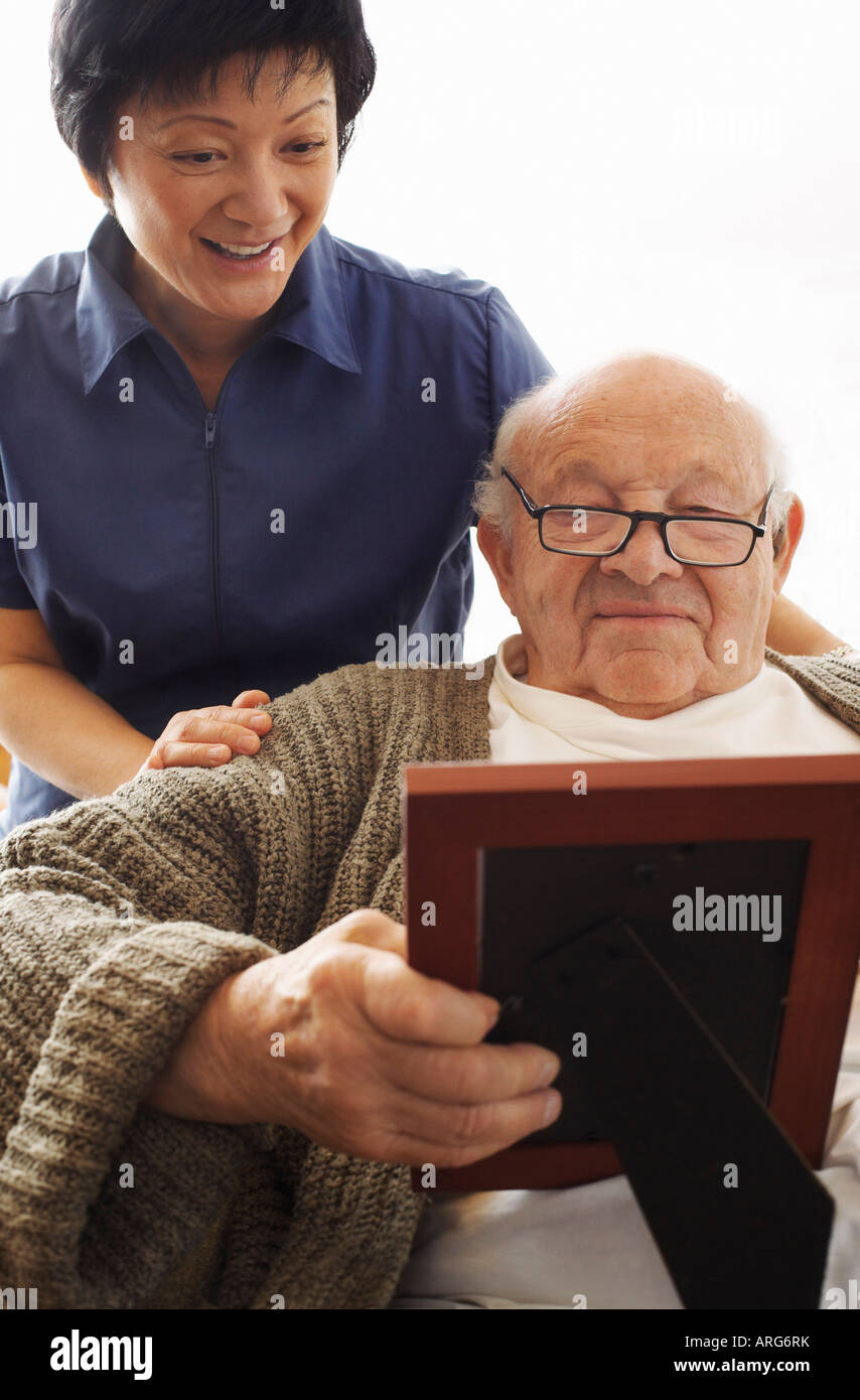 Senior Man Looking at Picture with Woman Looking over his Shoulder Stock Photo