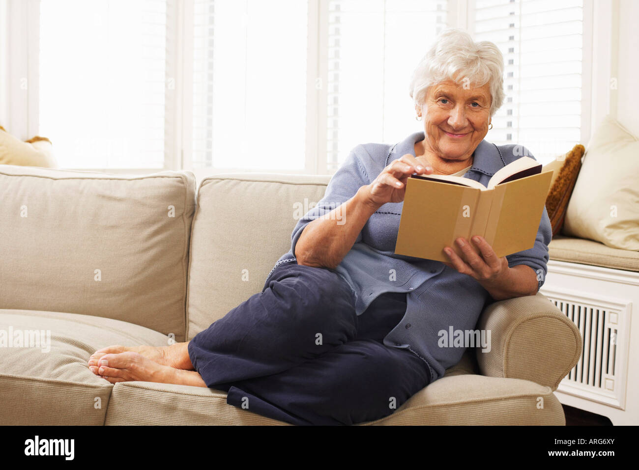 Senior Woman Sitting on Sofa Reading Book Stock Photo - Alamy