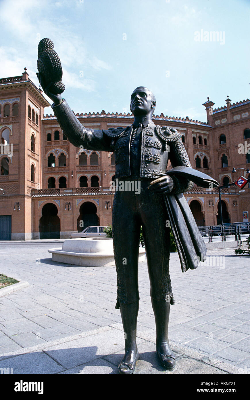A bronze statue of a bull fighter with hat in hand and cloak draped over his arm situated in Madrid s Calle de Alcala with the facade and towers of a building in the background Stock Photo