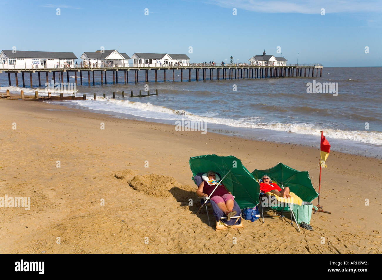 Two english women brave the english summer sun sunshine in deckchairs on the beach with blue sky in Southwold Suffolk UK Stock Photo