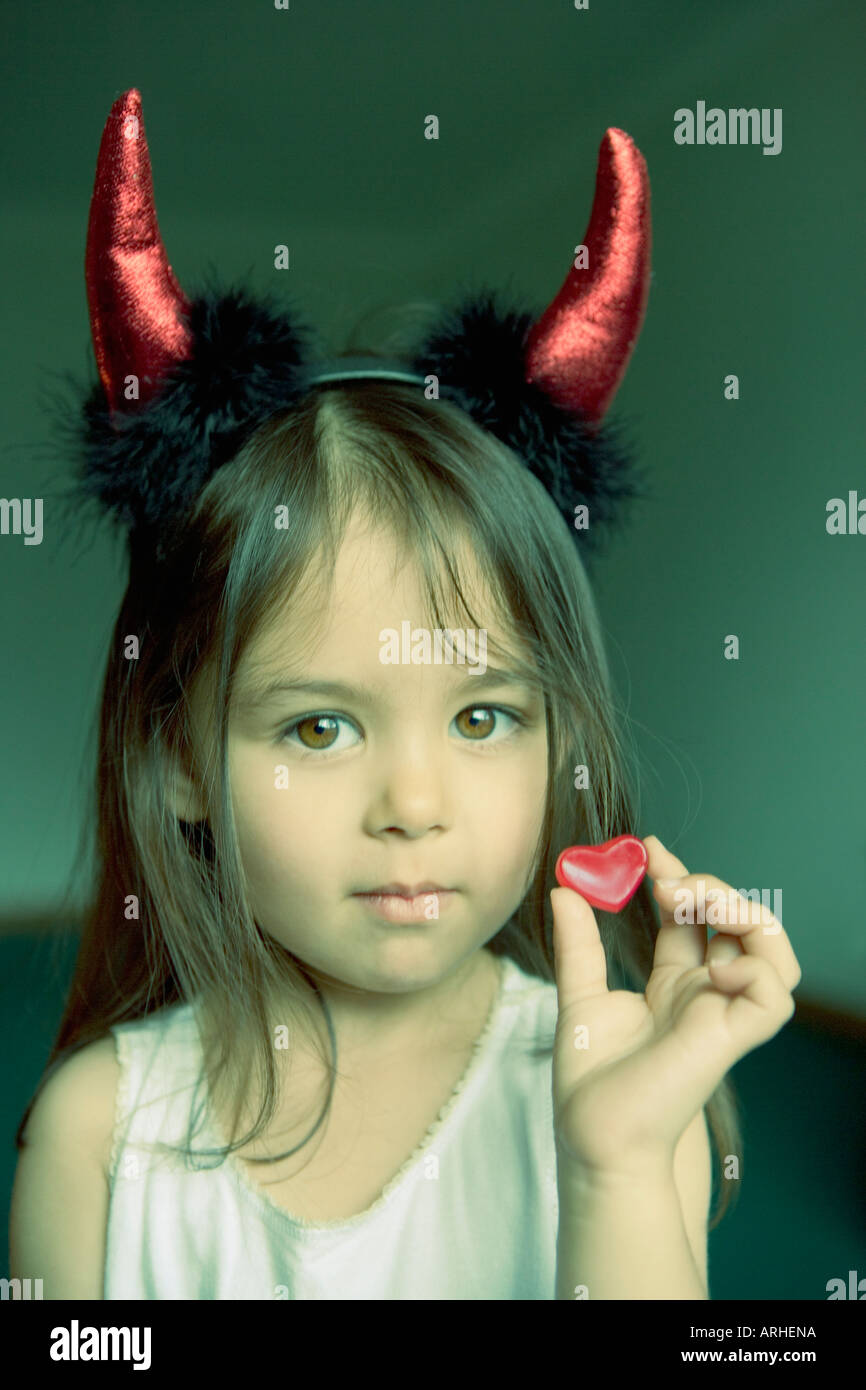 Pretty little girl with devil horns holds heart shaped sweet in hand