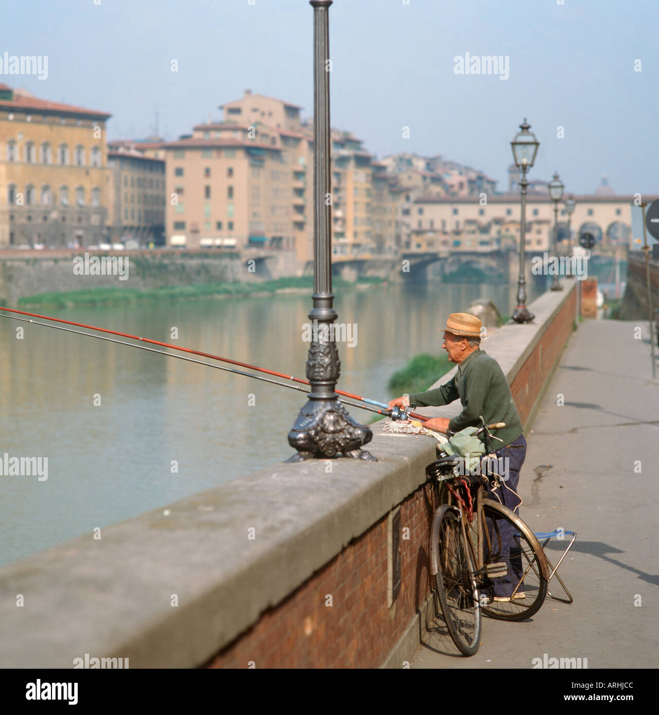 An old man fishing on the banks of the River Arno with the Ponte Vecchio in the distance, Florence, Tuscany, Italy Stock Photo