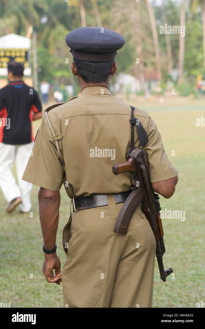 A Sri Lankan policeman with a gun watches a cricket game Stock Photo
