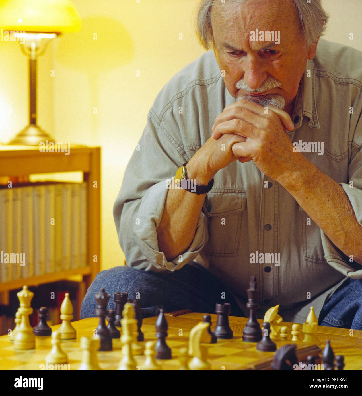 old man playing chess sitting in front of chessboard thinking reflecting reasoning Stock Photo