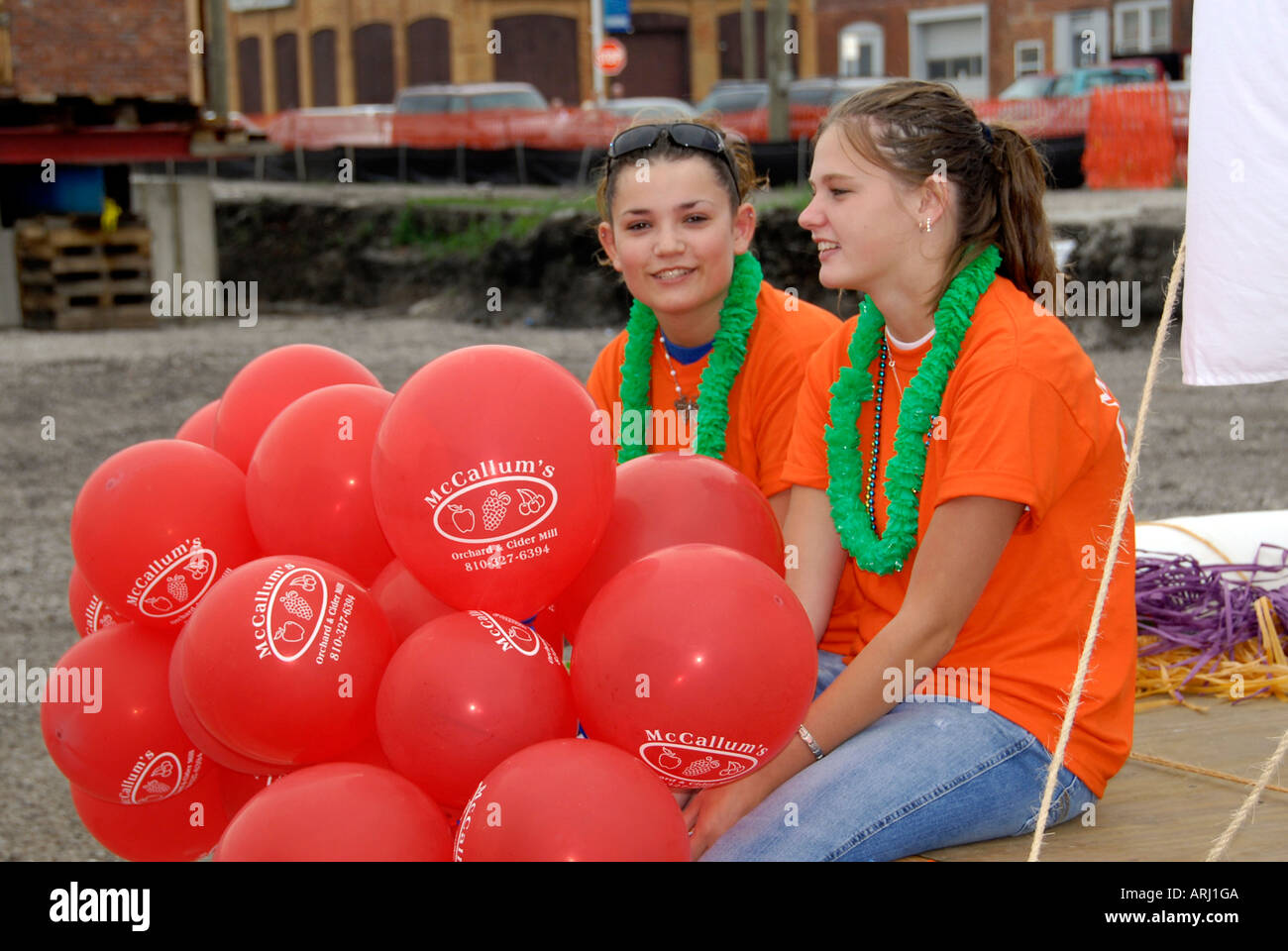Teen girls sit talking to one another while giving away free red balloons Stock Photo