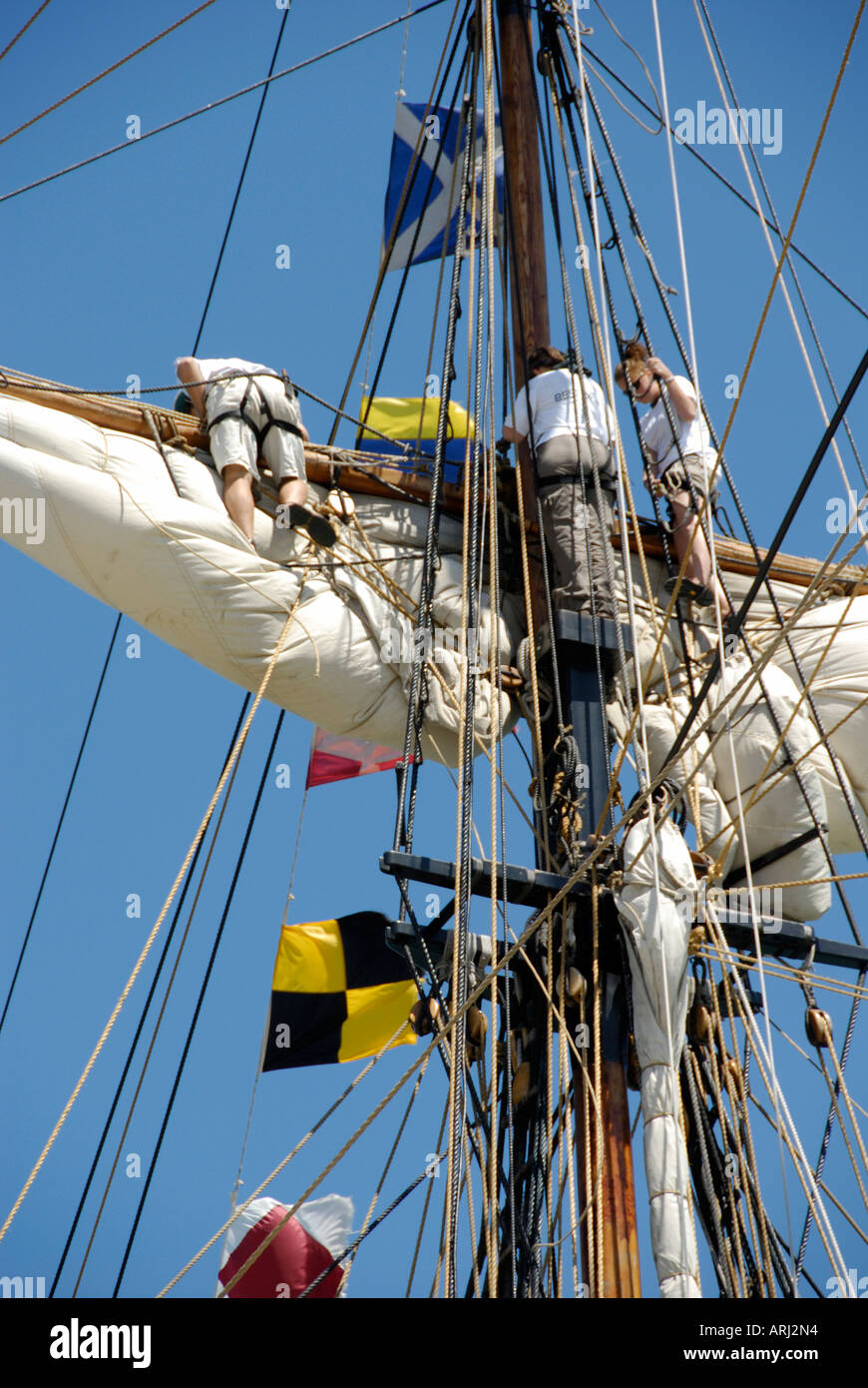 Sailors climb the mast of a tall sailing ship to effect maintenance and