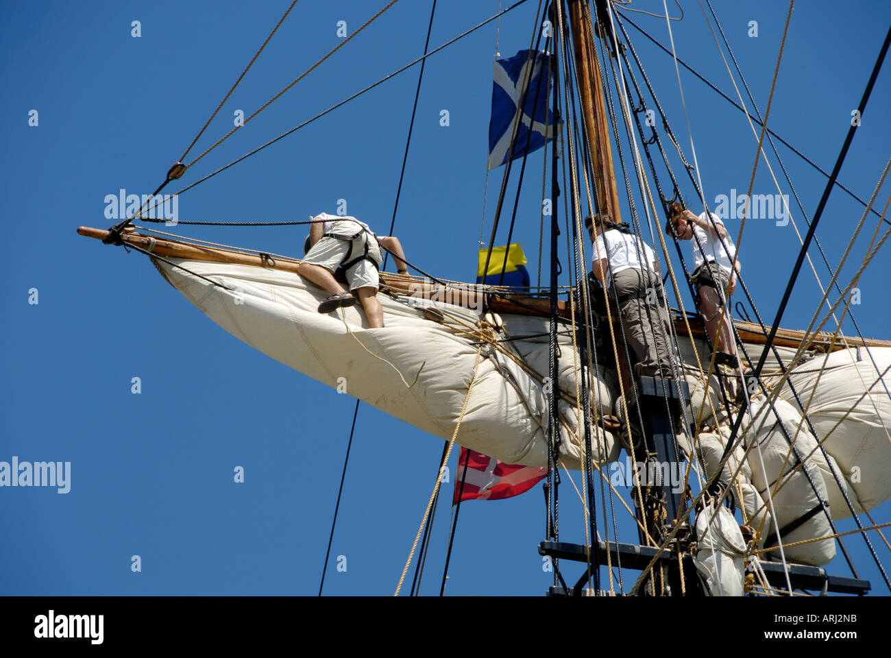 Sailors climb the mast of a tall sailing ship to effect maintenance and