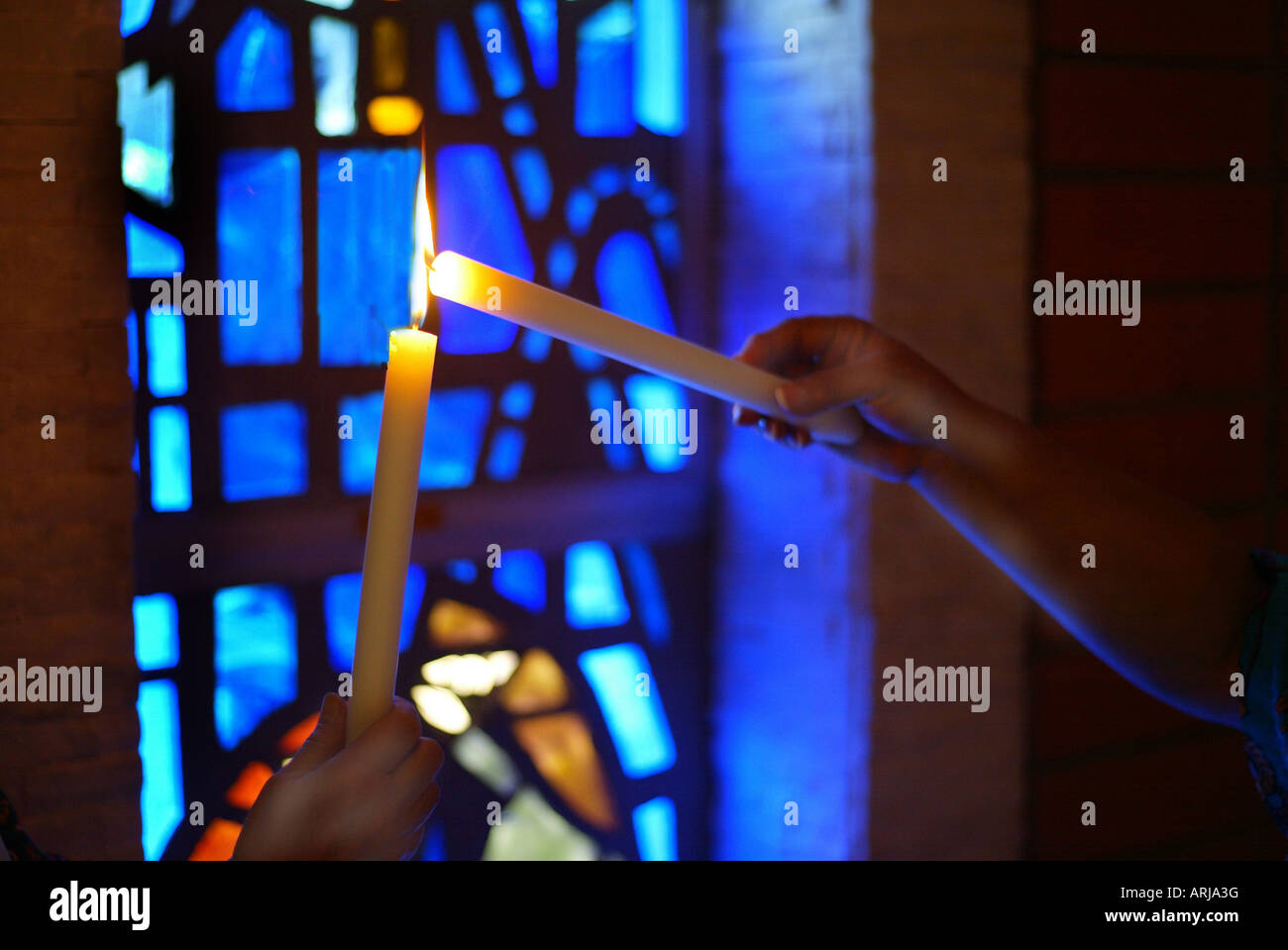 One white candle lights another in front of stained glass window Stock
