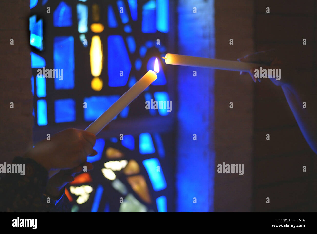 One candle lights another in front of stained glass window Stock Photo