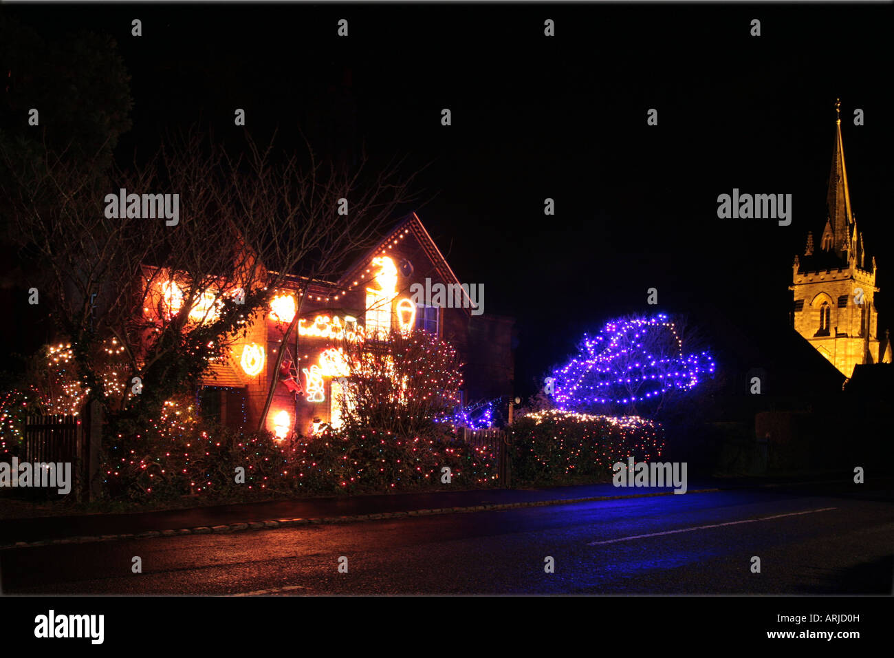 House festooned with Christmas lights with a floodlit church in