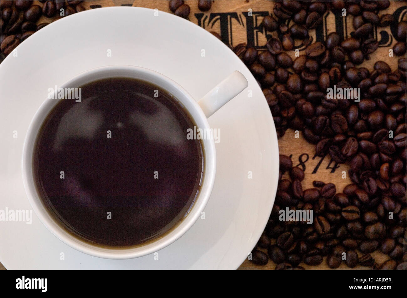 A close up of freshly made cup of coffee on a saucer, surrounded by roasted coffee beans on a antique wooden surface Stock Photo