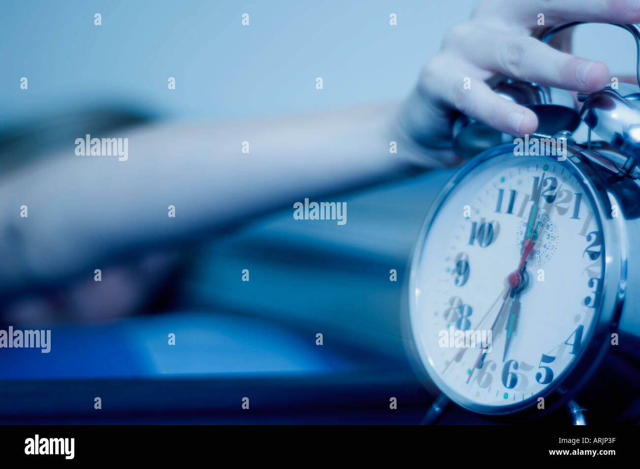 Young Woman reaching for a Ringing Alarm clock showing just after 6 am with fresh and modern toning Stock Photo