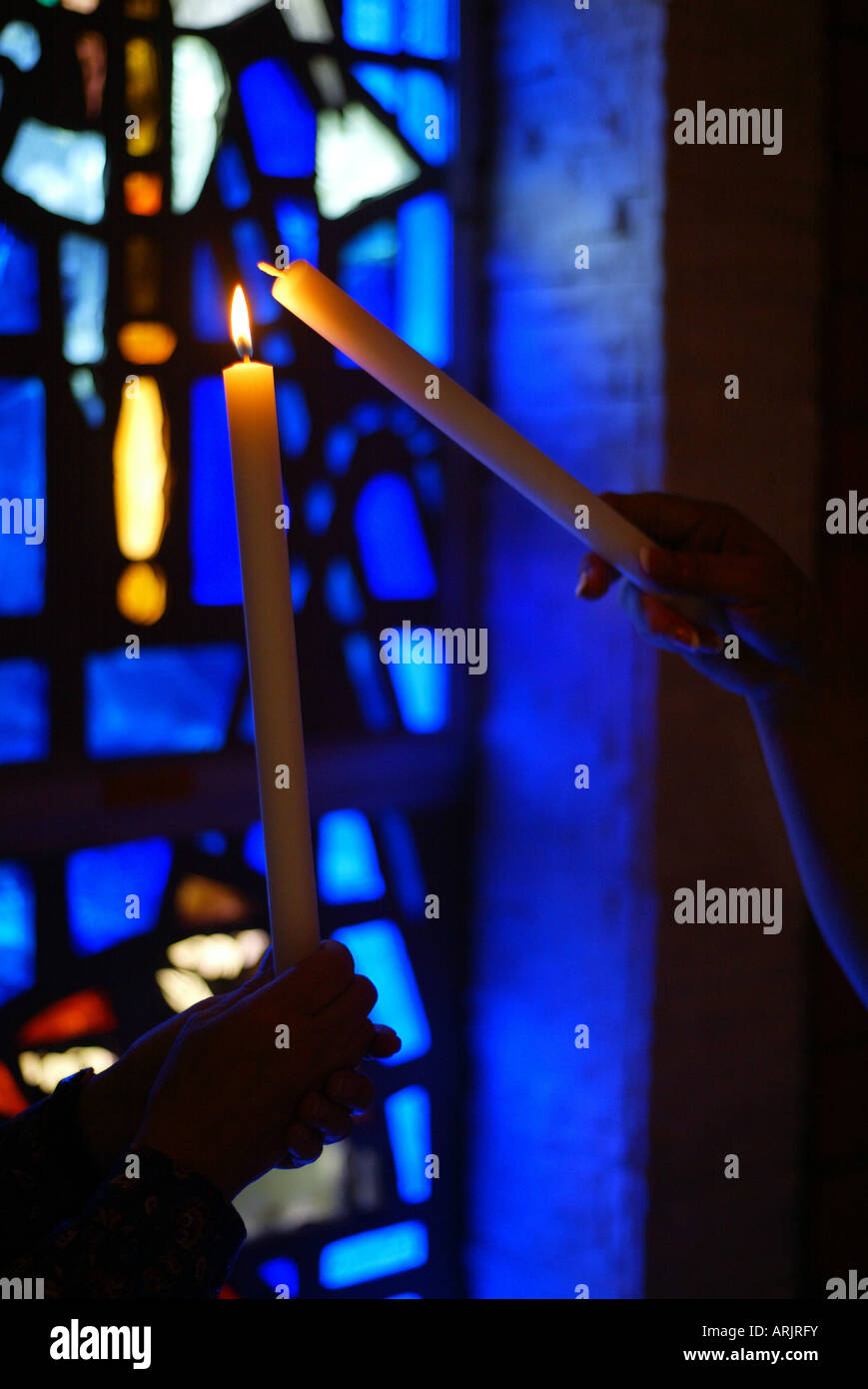 One candle lights another in front of stained glass window Stock Photo